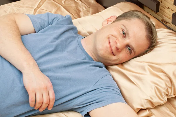 Muž ležící ložnici a usmívá se — Stock fotografie