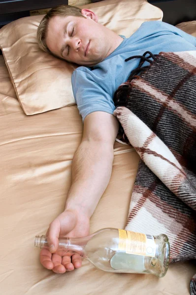 Молодой человек спит на диване с бутылкой виски — стоковое фото