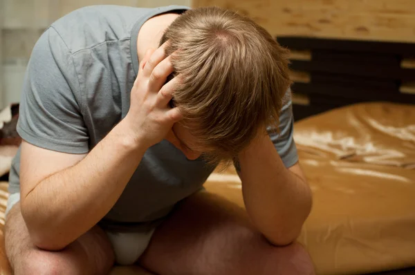 Молодой человек в депрессии сидит на кровати — стоковое фото