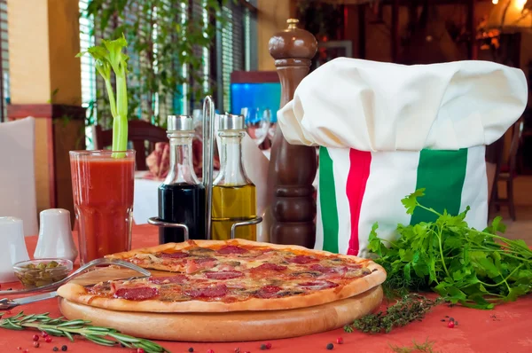 Fecho de uma mesa com pizza e chapéu de cozinheiro — Fotografia de Stock