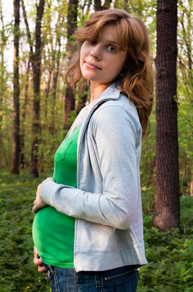 Feliz joven embarazada sosteniendo sus manos sobre su barriga — Foto de Stock