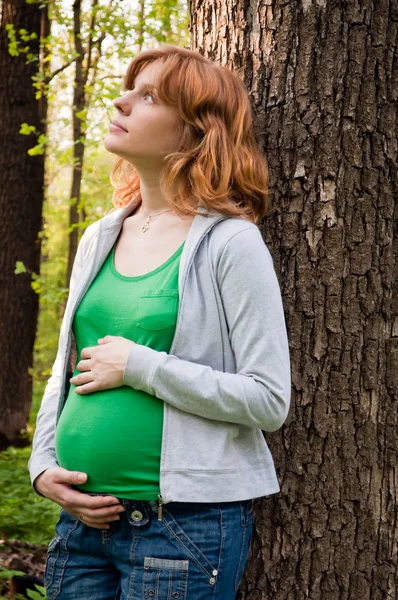 Glückliche junge schwangere Frau hält ihre Hände auf ihrem Bauch — Stockfoto