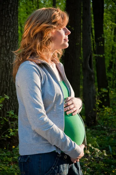 Gelukkig jonge zwangere vrouw die haar handen op haar buik — Stockfoto