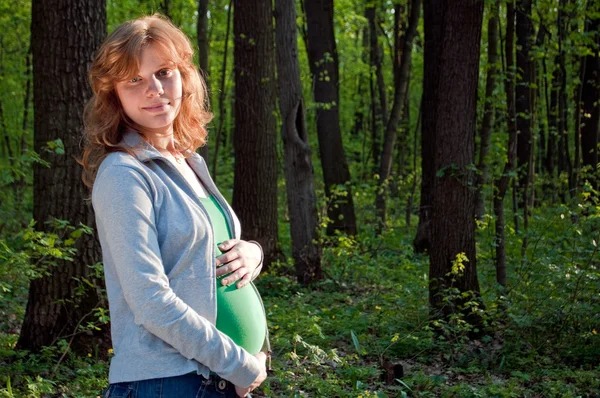 Feliz jovem grávida segurando as mãos em sua barriga — Fotografia de Stock
