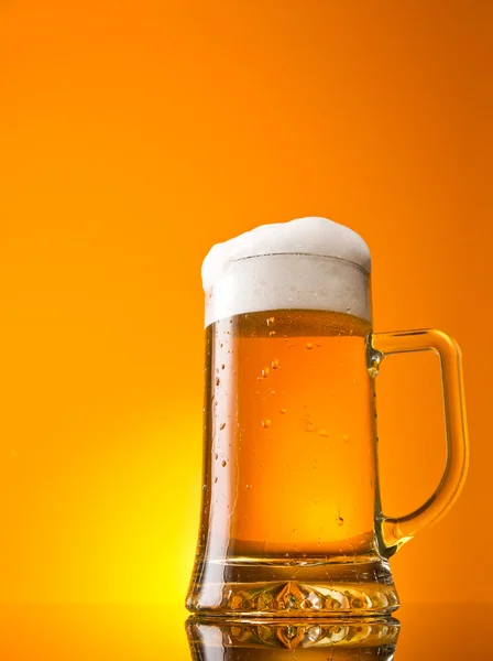 Vaso de cerveza en primer plano con espuma sobre fondo naranja — Foto de Stock