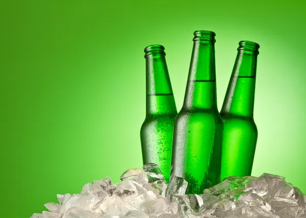 Three beer bottles getting cool in ice cubes. Isolated on a gree — Stock Photo, Image
