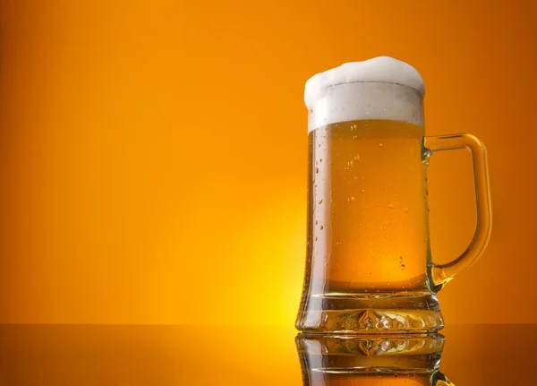 Стакан пива крупным планом с пеной на оранжевом фоне — стоковое фото