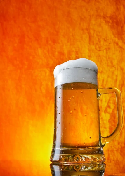 Стакан пива крупным планом с пеной на оранжевом фоне — стоковое фото