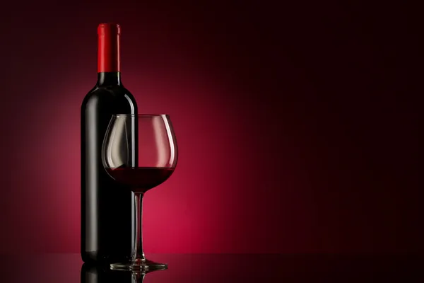 Láhev červeného vína a skla na červený gradient — Stock fotografie