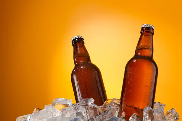 Δύο μπουκάλια μπύρας να πάρει δροσερό σε παγάκια. απομονωμένη σε ένα πορτοκαλί. — Φωτογραφία Αρχείου