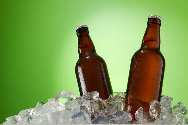 Δύο μπουκάλια μπύρας να πάρει δροσερό σε παγάκια. απομονωμένη σε ένα πράσινο. — Φωτογραφία Αρχείου