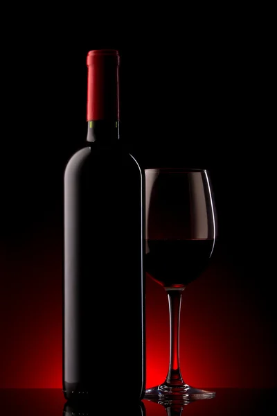 Fles met rode wijn en een glas op een rood kleurverloop — Stockfoto