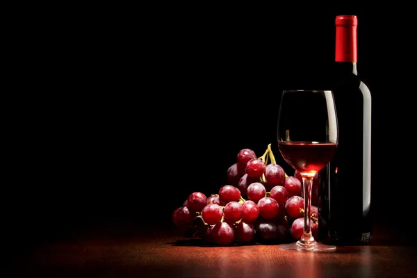 Glas wijn en fles en rode druiven op een houten tafel — Stockfoto
