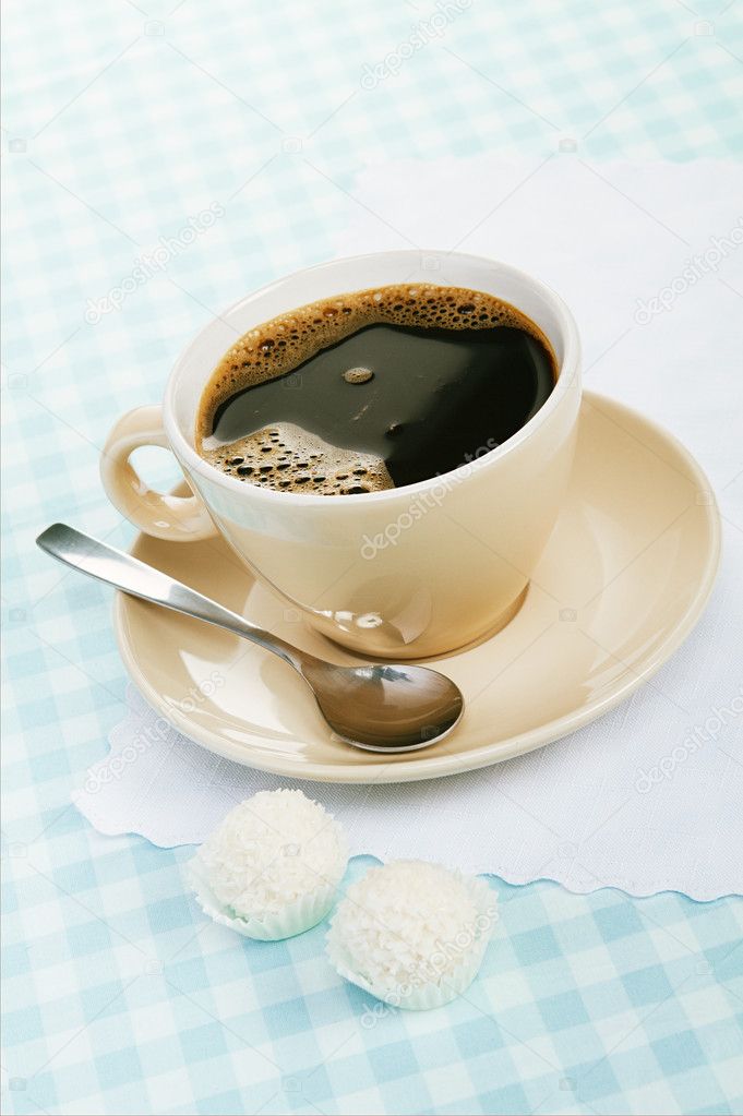 Black coffee with coconut candies on a blue tablecloth