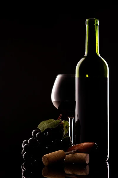 White bottle with red wine and glass and cork with a corkscrew on a black