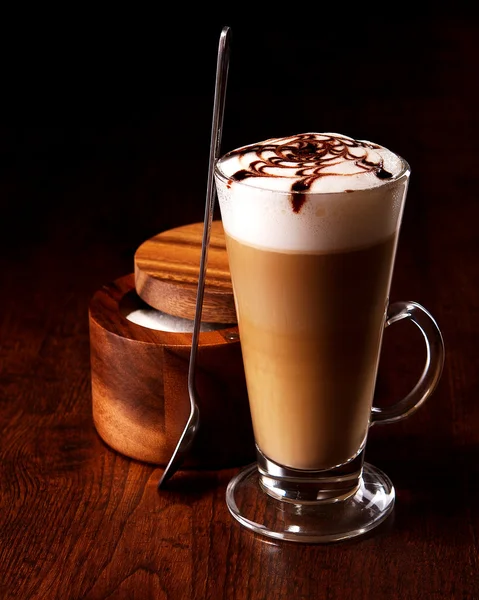 Taza de café con leche en una mesa de madera con una cuchara y azúcar — Foto de Stock