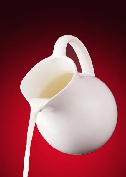 Pitcher of milk on a red background — Stock Photo, Image