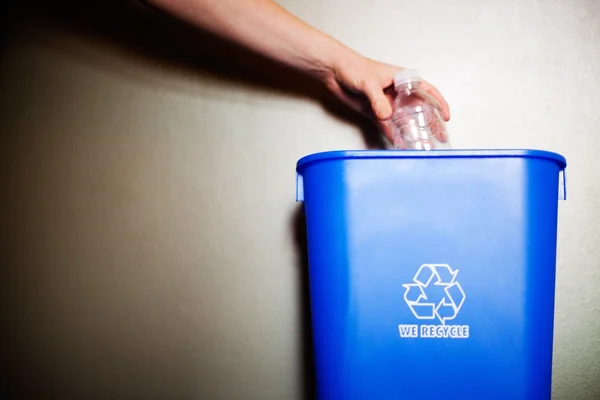 Braço deixando cair o engarrafamento plástico no recipiente de reciclagem Imagens Royalty-Free