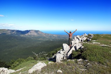 Sports man costs on a rock, having lifted upwards hands clipart