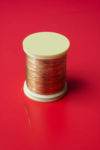 Bobbin of golden thread on a red background — Stock Photo, Image