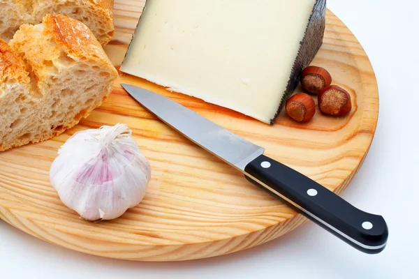 Cheese, bread, hazelnuts and knife on wood plate — Stock Photo, Image