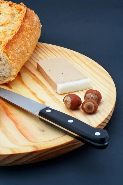 Paštika, chléb, lískové ořechy a nůž na dřevěné desce — Stock fotografie