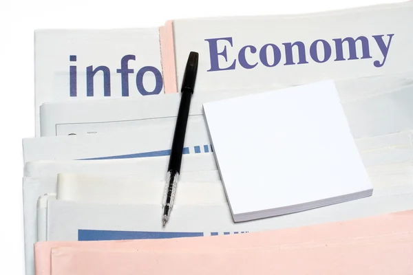 Note and pen, over stacked economy newspapers — Stock Photo, Image