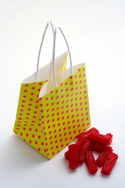 Saco de compras amarelo e pedaços de licorices vermelhos — Fotografia de Stock