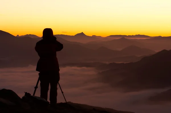 Silhouette del fotografo sopra una montagna nebbiosa — Foto Stock