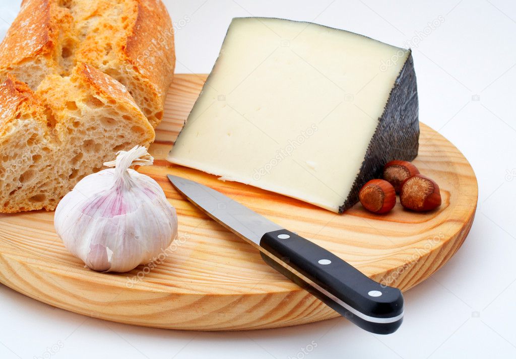 Cheese, bread, hazelnuts and knife on wood plate