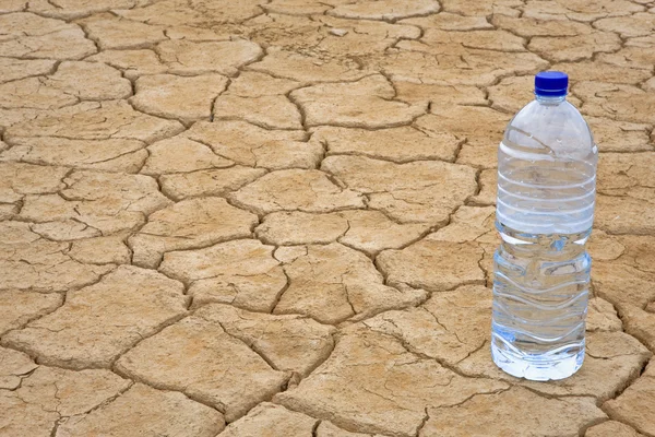 Botella de agua en tierra seca — Foto de Stock