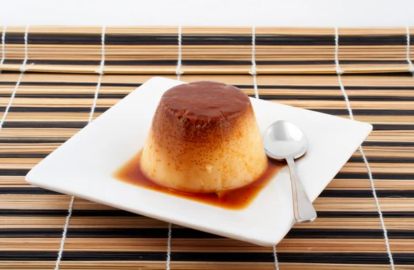 Crema alla vaniglia e dessert al caramello con cucchiaio su piatto bianco — Foto Stock
