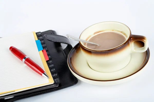 Primer plano de una taza de café con la cuchara dentro y cuaderno con ballpoi —  Fotos de Stock