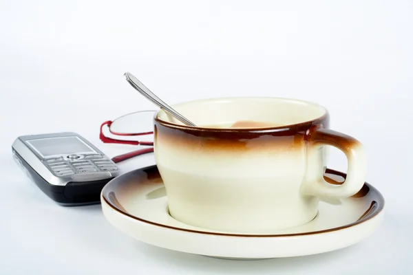 Närbild av en kopp kaffe med sked inne, mobiltelefon och par — Stockfoto