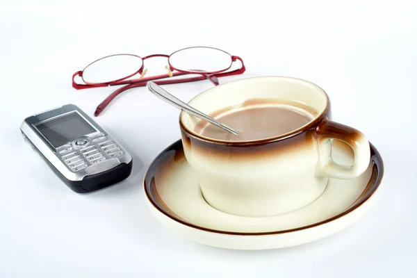 Close-up of a cup of coffee with the spoon inside, cellular phone and pair — Stock Photo, Image