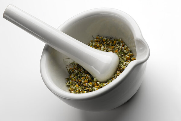 White marble mortar and pestle with chamomile inside