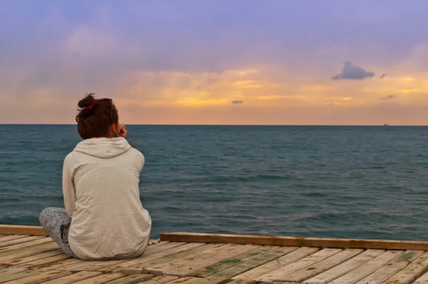 Das Mädchen blickt auf den Sonnenuntergang am Meer — Stockfoto