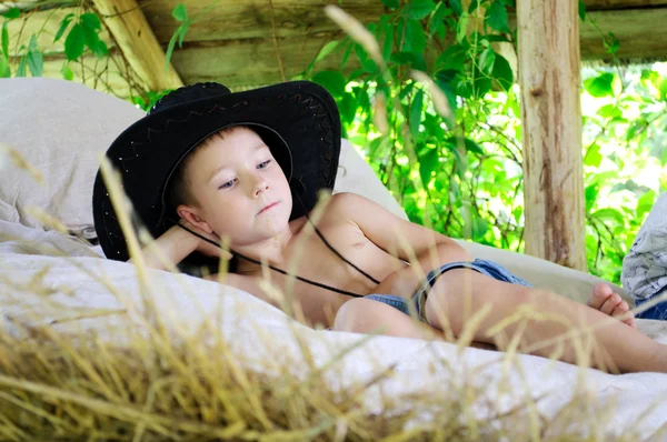 Niño en un sombrero de vaquero está en el pajar —  Fotos de Stock