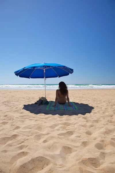Guarda-sol azul com mulher sentar na toalha — Fotografia de Stock