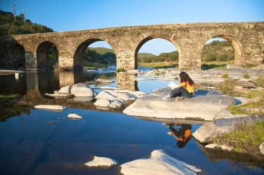 Woman reading next to a river clipart