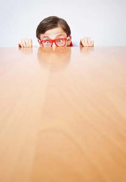 Nerd asustado escondido detrás de un escritorio —  Fotos de Stock