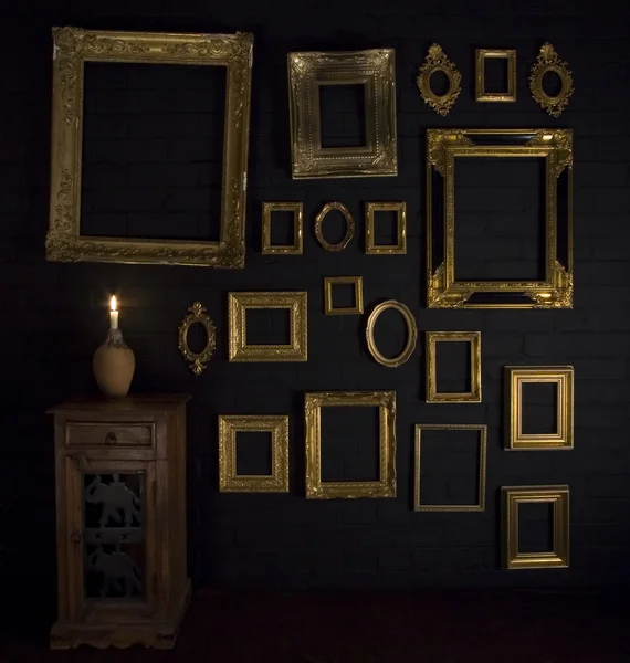 Gold frames on a black brick wall and candle — Stock Photo, Image