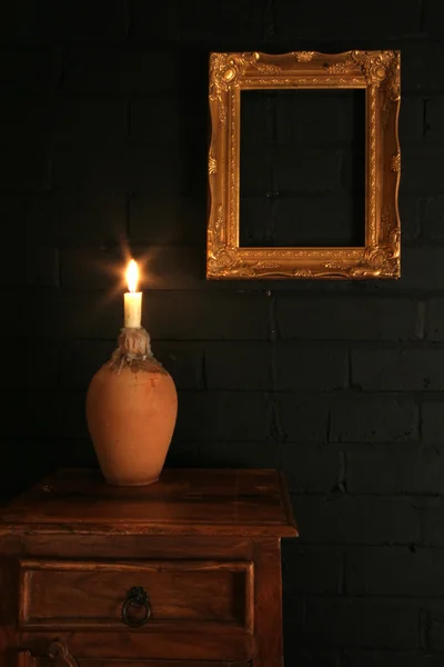 Gold frame on a black brick wall and candle — Stock Photo, Image