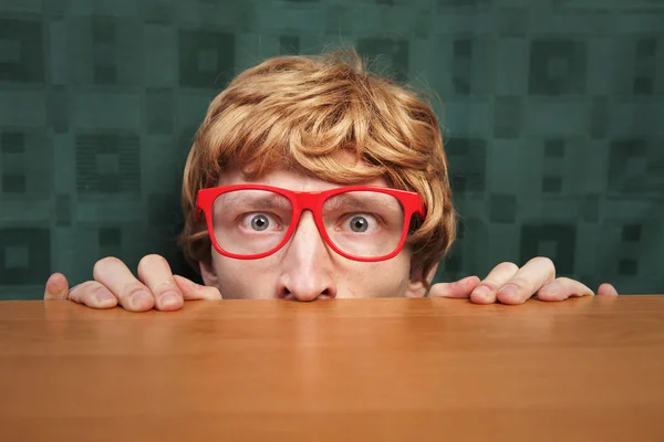 Un nerd effrayé caché derrière un bureau — Photo