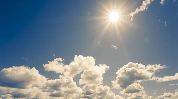 Bright sun on blue sky with fluffy clouds — Stock Photo, Image