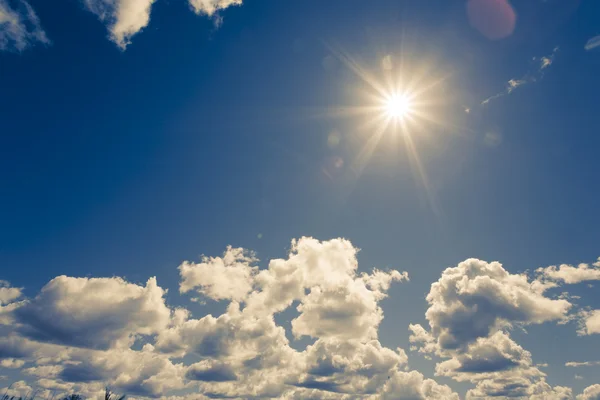 Bright sun on blue sky with fluffy clouds — Stock Photo, Image