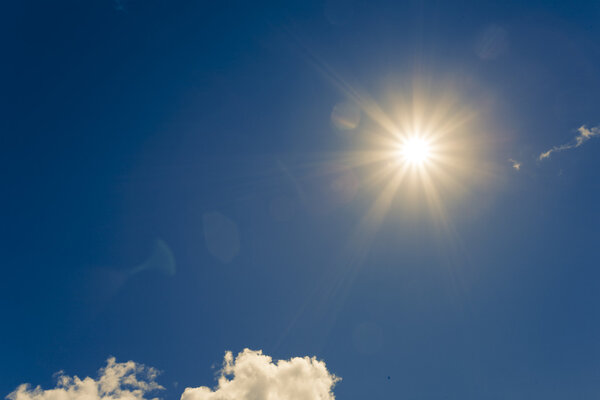 Яркое солнце на голубом небе с пушистыми облаками

