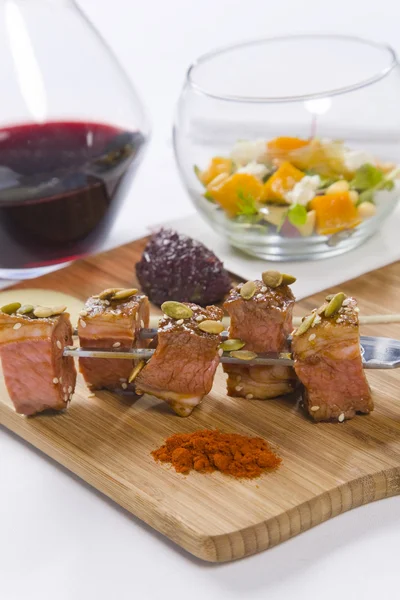 Beef served on skewers with condiments and red wine — Stock Photo, Image