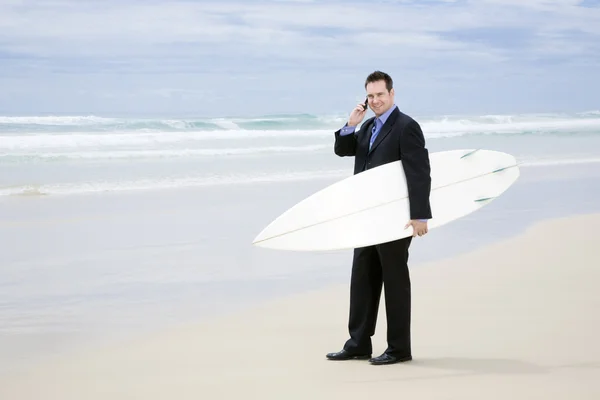 stock image Business man in suit walking with surfboard on the beach