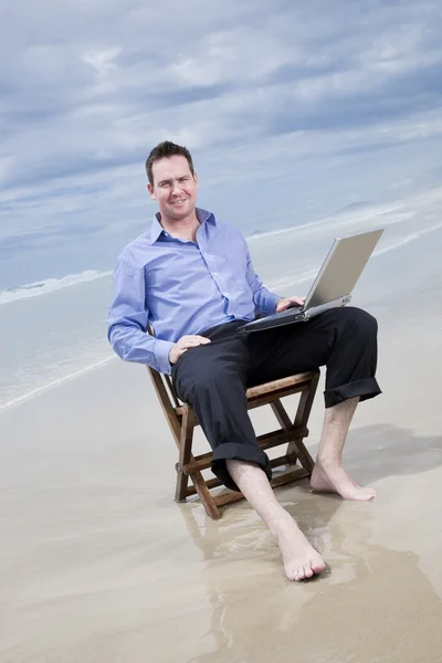 Biznes człowiek siedzi na krześle na plaży z laptopa — Zdjęcie stockowe